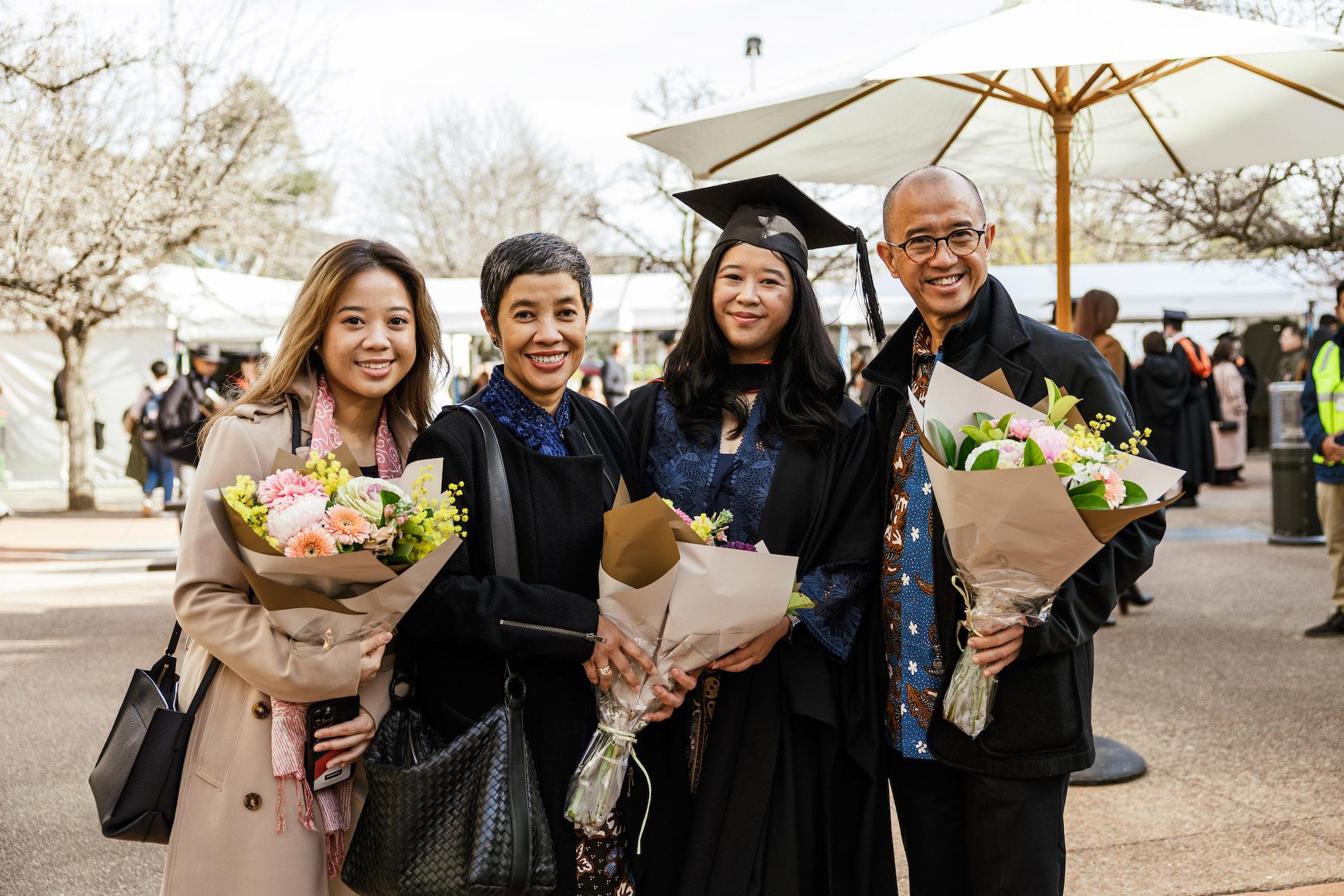 A family from the CAP graduations standing outdoors holding flowers and smiling
