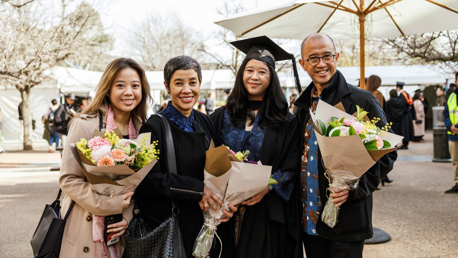 A family from the CAP graduations standing outdoors holding flowers and smiling